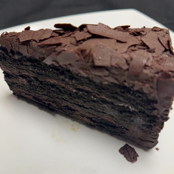 A rich, dark chocolate cake slice with chocolate shavings on top, on a white plate.