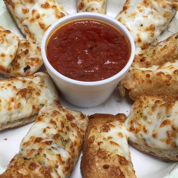Cheesy garlic breadsticks with melted mozzarella and golden crust, surrounding a cup of marinara sauce.