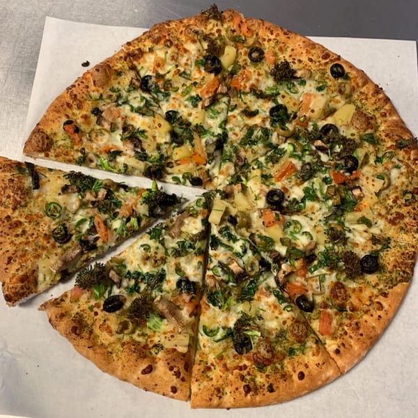 A freshly baked Pizza And Grill pizza, topped with vegetables, cheese, and olives, with one slice removed.