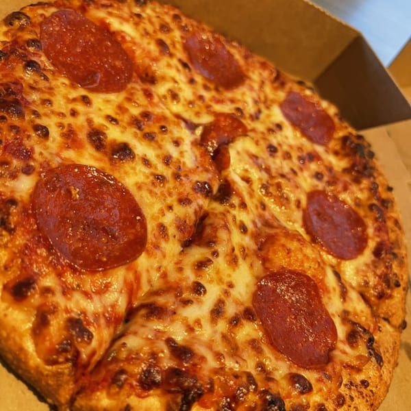 Close-up of a hot, cheesy pepperoni pizza from Pizza And Grill in a cardboard box.