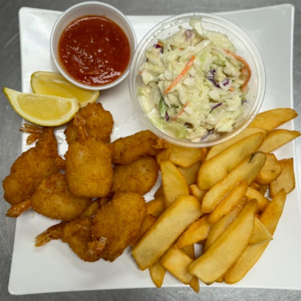 Fried shrimp, steak fries, coleslaw, cocktail sauce, and lemon wedges on a white plate.